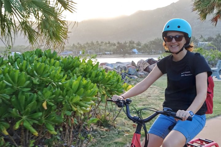 Person with blue helmet rides red bike on path through tropical scenery.